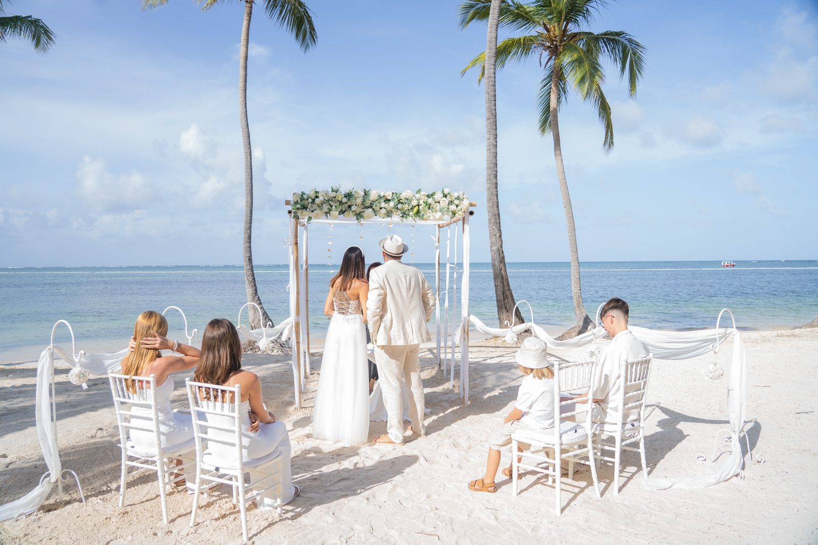 Small beach wedding ceremony under a floral arch by the ocean