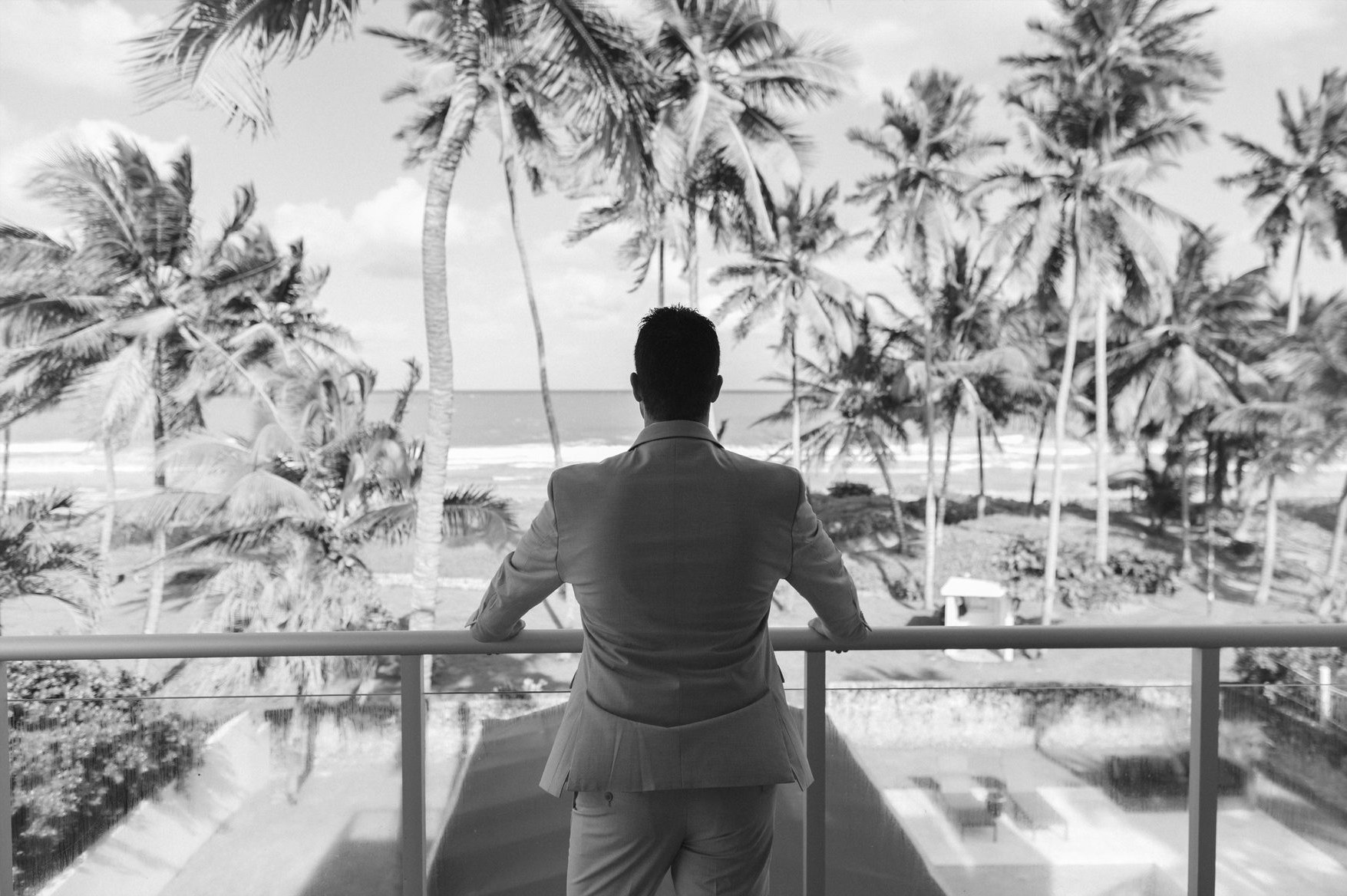Groom looking out over the ocean and palm trees from a balcony in the Dominican Republic